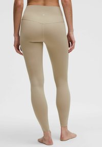 Leggings beige a vita alta con una texture liscia, design aderente e dettagli di cucitura discreti sul retro, che si estendono fino alle caviglie.