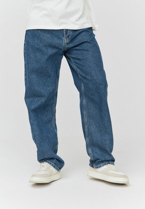 Jean en denim bleu avec une coupe décontractée, jambes droites et un léger délavage. Associés à des baskets blanches et beiges avec un design texturé.