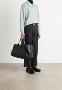 Svart läder duffelväska med rund form, dubbla handtag och en sidodragkedja. Bärs med en ljusblå, oversized tröja och svarta byxor.