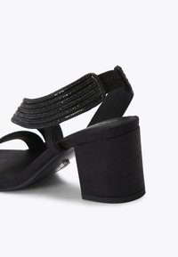 Zwarte open-toe sandalen met hak, voorzien van een gestructureerde band met kraalaccenten, een suede-achtige stof en een chunky blokhak.