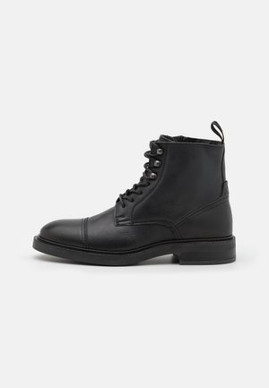Sort læderankelstøvle med snøreforside, rund tå, lav hæl og trækkrog bagpå, vist i sideprofil på hvid baggrund.