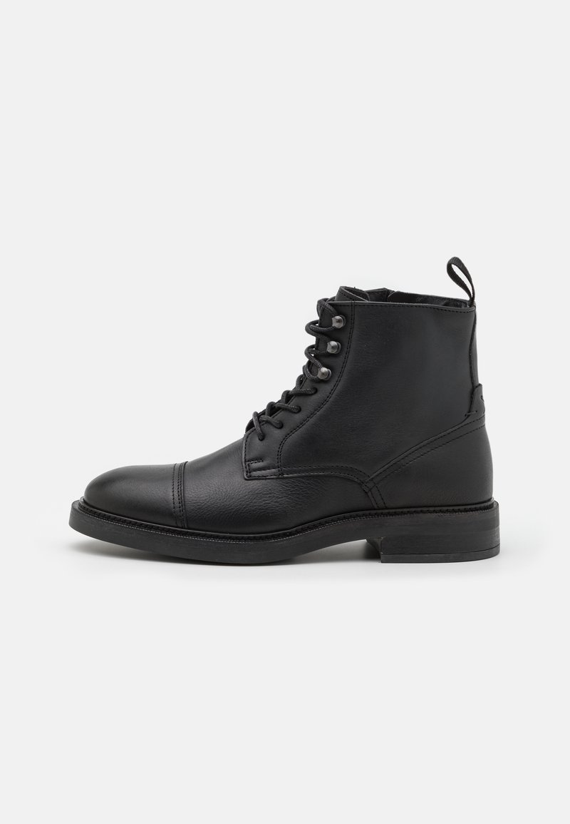 Bottine noire en cuir avec lacets sur le devant, bout rond, talon bas et languette à l'arrière, présentée de profil sur fond blanc.