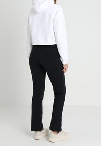 Felpa bianca a mezzaluna con cappuccio, abbinata a pantaloni neri aderenti. L'outfit presenta una superficie liscia e colori neutri.