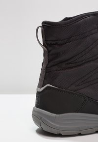 Schwarzer High-Top-Sneaker mit strukturiertem Obermaterial, glatter schwarz-grauer Sohle und einem Zugtab hinten für einfaches An- und Ausziehen.