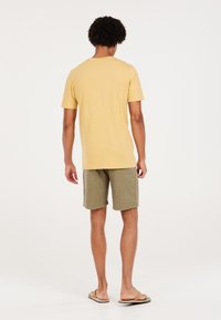 Geel katoen T-shirt met korte mouwen, gecombineerd met olijfgroene gebreide shorts. Sandalen maken de casual look compleet.