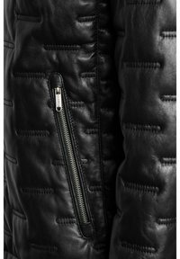 Must musta nahkjakker, millel on tekstureeritud, tikkitud muster. Esiosas on hõbedane tõmblukk ja ühtlase värvusega õmblustead. 