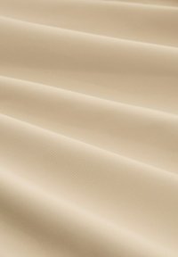 Beige stof met een gladde, matte textuur, gekenmerkt door zachte, vloeiende plooien die zachte schaduwen en highlights creëren.