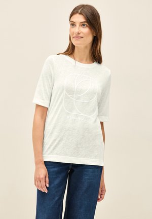 T-shirt gris clair à manches courtes en tissu doux et texturé, ornée d'un design géométrique blanc avec du texte en dessous, associée à un pantalon en denim foncé.