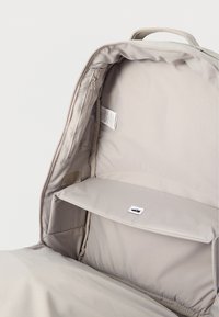 Εσωτερικό ανοιχτού μπεζ σακιδίου πλάτης που δείχνει ένα κύριο διαμέρισμα με επενδυμένη θήκη για φορητό υπολογιστή και μια μικρή τσέπη με φερμουάρ στην πλευρά.