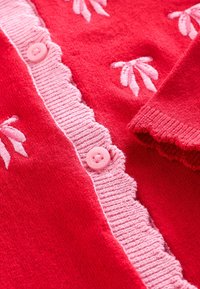 Roter Strickcardigan mit rosa gewelltem Rand, rosa Knöpfen und bestickten Blattmustern. Weiche Textur und sorgfältige Verarbeitung.