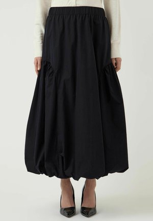 Czarna spódnica balonowa z marszczonym dołem, noszona z czarnymi butami na szpic oraz kremową bluzką z długim rękawem, pokazana od talii do stóp.