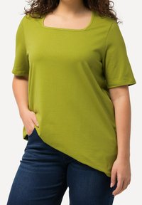 Top verde a maniche corte con scollo quadrato e vestibilità rilassata. Realizzato in tessuto morbido, presenta un orlo curvo e dettagli con tasche laterali.