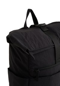 Juodas suvolkamas kuprinės modelis, pagamintas iš tekstūruotos medžiagos, su sagties uždarymu, šoniniu užtrauktuku ir viršutine nešimo rankena.