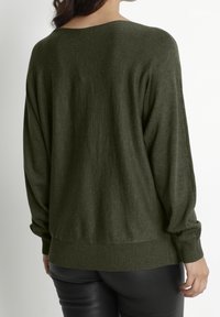 Olivgrön, oversized tröja med ett mjukt, texturerat tyg. Har en vid halsringning samt ribbade detaljer vid ärmsluten och fållen. Bakvy.