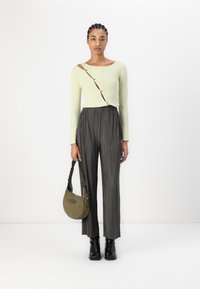 Pull côtelé vert clair avec un décolleté large, associé à un pantalon plissé noir. Sac à épaule vert olive et bottines noires.
