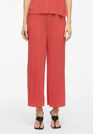 Pantaloni larghi rossi plissettati con una finitura texturizzata, dotati di una vita media e di una vestibilità ampia, abbinati a sandali neri.