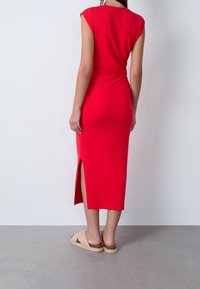 Robe midi rouge sans manches avec des fentes latérales, mettant en avant une silhouette ajustée et une texture lisse. Assortie avec des sandales à plateforme de couleur claire.