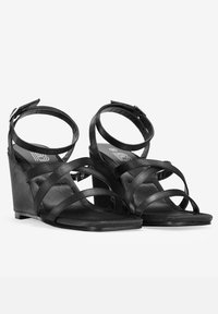 Sandalias de cuña negras con tiras entrelazadas, correas para el tobillo con hebillas y un acabado mate suave. Punta cuadrada y suela texturizada.