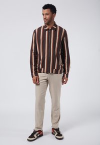 Brun randig zip-up-jacka med krage och framficka, matchad med ljusbeige byxor och flerfärgade sneakers.