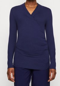 Marinblå långärmad omslagstopp i mjukt material, med en djup V-halsringning, sidofållning och en slät yta. Bärs med matchande byxor.