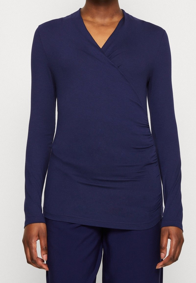 Marinblå långärmad omslagstopp i mjukt material, med en djup V-halsringning, sidofållning och en slät yta. Bärs med matchande byxor.