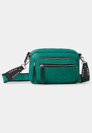 Modrozelená kožená crossbody taška s předním zipovým kapsou, nastavitelným černým popruhem se stříbrnými cvoky a vyraženým logem na přední kapse.