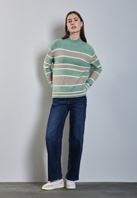 Hellgrüner und beiger gestreifter Strickpullover mit hohem Kragen, kombiniert mit dunkelblauen gerade geschnittenen Jeans und weißen Sneakers.