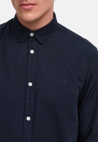 Chemise boutonnée bleu marine en mélange de coton, avec un col classique, des boutons blancs et un petit logo brodé sur le côté gauche.