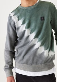 Felpa tie-dye verde e grigia con polsini e orlo a coste, caratterizzata da una toppa quadrata con logo sul petto. Realizzata in materiale cotone.