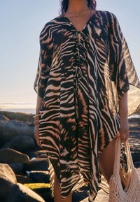 Schwarz-beiger Kaftan mit Zebramuster, V-Ausschnitt, verstellbarem Bindverschluss und weiten Ärmeln. Leichter, transparenter Stoff.