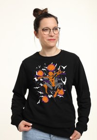 Svart sweatshirt med en grafik av Spider-Man omgiven av pumpor och fladdermöss, med färgglada detaljer i orange, lila och vitt.