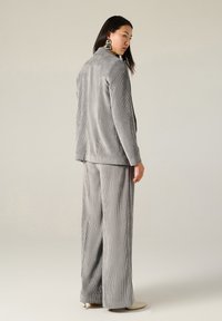 Completo in velluto a coste grigio con giacca su misura e pantaloni a gamba larga. Presenta righe verticali e una texture liscia. Tacchi a stiletto completano l'outfit.