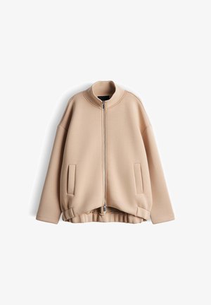 Beige Reißverschlussjacke mit hohem Kragen, elastischem Saum, langen Ärmeln und zwei Fronttaschen, auf weißem Hintergrund dargestellt.