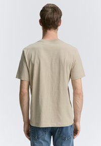 Beige katoenen t-shirt met korte mouwen, ronde halsontwerp en een relaxed fit, gezien vanaf de achterkant, gecombineerd met blauwe spijkerbroek.