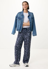 Veste en denim bleu clair, coupe ample, avec poches poitrine. T-shirt blanc en dessous, associé à un pantalon marine à motifs avec des accents floraux et cordon de serrage.