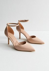 Nude patentleren hakken met spitse neus, enkelbandje en slanke 10 cm hoge stiletto. Glad textuur met een minimalistisch ontwerp en open zijkanten.