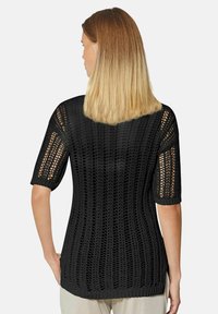 Schwarzer gestrickter Pullover mit kurzen Ärmeln, der ein Lochmuster und einen lässigen Schnitt aufweist. Das Material ist leicht und hat gerippte Akzente.