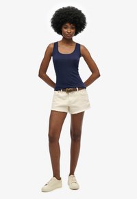 Granatowy top na ramiączkach, kremowe szorty z postrzępionym dołem, brązowy pasek, jasne sneakersy. Skup się na luźnym i wygodnym letnim stylu.