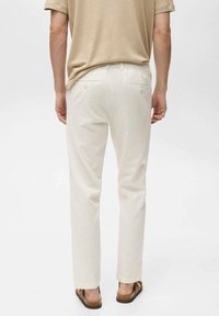 Męskie kremowe spodnie z subtelnym pionowym wzorem w paski, wyposażone w tylne kieszenie z jasnymi metalowymi elementami oraz prostą nogawką.
