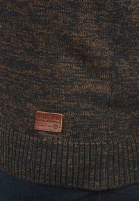 Strickpullover mit einem strukturierten Muster in Dunkelblau und Rost. Verfügt über ein braunes Lederetikett mit dem Markennamen "BLEND" am Saum.