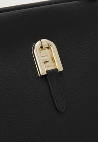 Sac en cuir noir texturé avec fermoir en métal doré et languette en cuir noir attachée au fermoir.