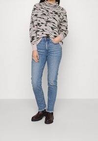 Gebreide trui in lichtroze met zwarte en groene abstracte patronen. Gecombineerd met lichtblauwe high-waisted jeans en donkerbruin enkellaarsjes.