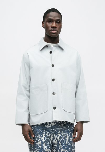 Veste boutonnée gris clair avec col, deux poches avant et coupe décontractée. Présente une texture lisse et des détails de coutures discrètes.