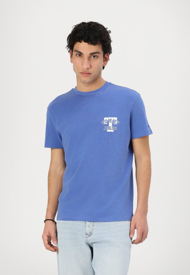 Zils kokvilnas T-krekls ar apaļu kakla izgriezumu un īsām piedurknēm, ar mazu baltu "TOMMY JEANS" logo kreisajā krūšu daļā.