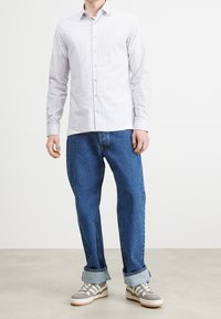 Bílé a světlé šedé pruhované košile s dlouhými rukávy, spárované s volnými džínovými kalhotami a šedými teniskami s bílými podrážkami.