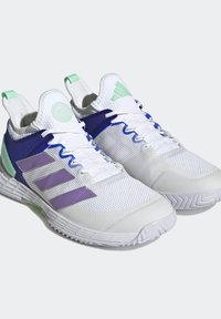 Białe buty sportowe z siateczkową cholewką, fioletowymi i niebieskimi akcentami, zielonymi detalami oraz teksturowanymi podeszwami dla lepszej przyczepności. Sznurowana konstrukcja z uchwytami.
