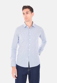 Camicia a maniche lunghe a righe in azzurro chiaro e bianco, con colletto button-down e maniche con polsini, abbinata a jeans scuri.