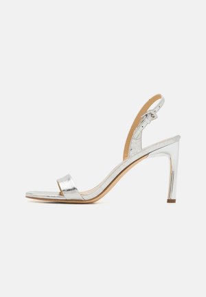 Sølvmetallic højhælet sandal med ankelstrop, åben tå og slank hæl på hvid baggrund.