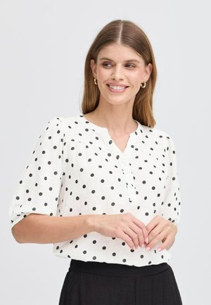 White blouse with black polka dots, round neckline, short puff sleeves, and button detail. Textured fabric adds visual interest.
