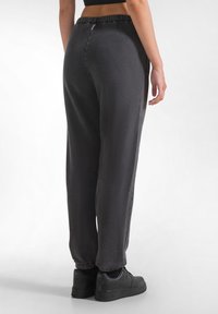 Schwarze Fleece-Jogginghosen mit lockerem Schnitt, elastischem Bund, eng zulaufenden Knöcheln und glatter Textur, kombiniert mit schwarzen Sneakers.